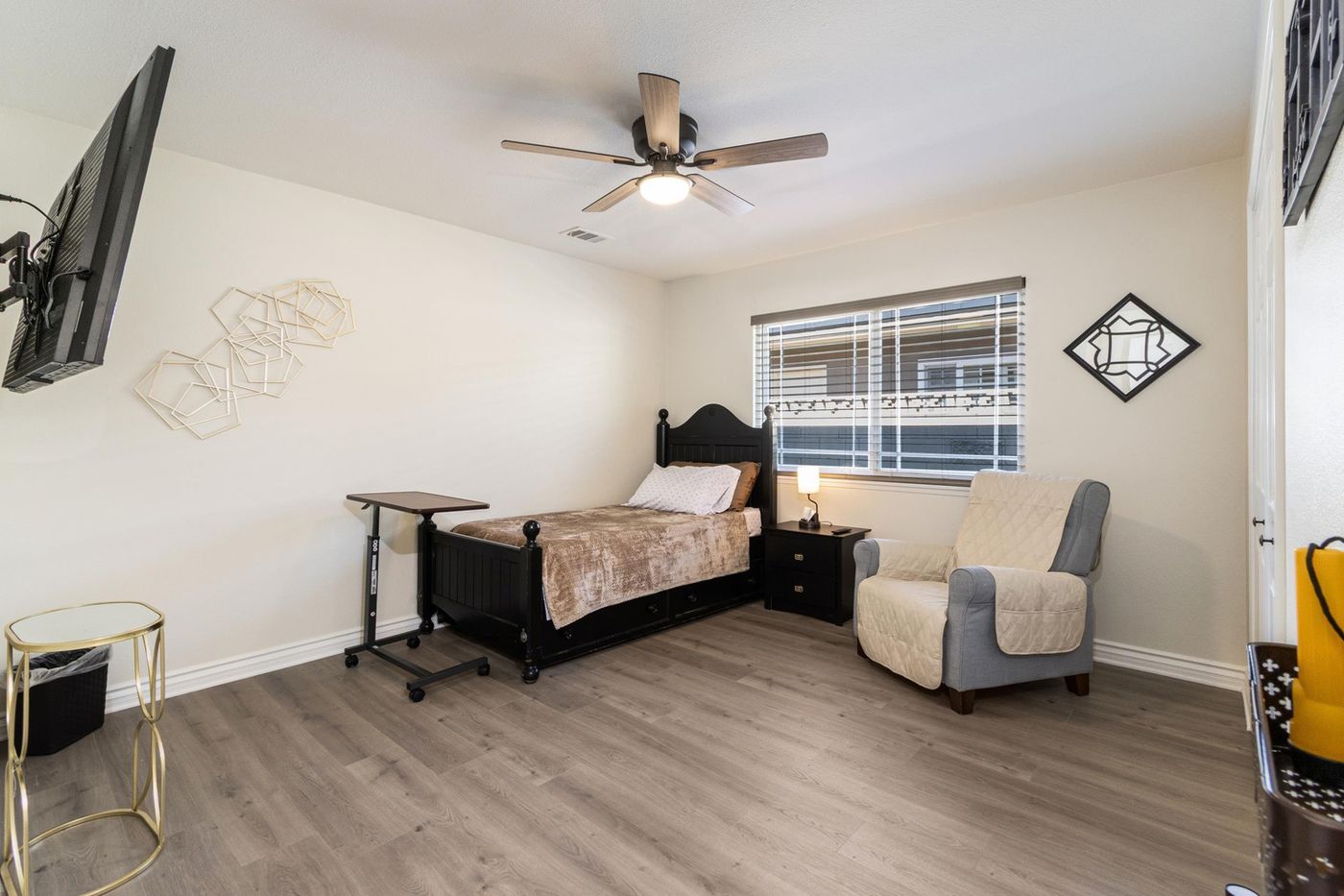 A private bedroom with a bed, a nightstand, a lounge chair, a ceiling fan and a wall-mounted TV
